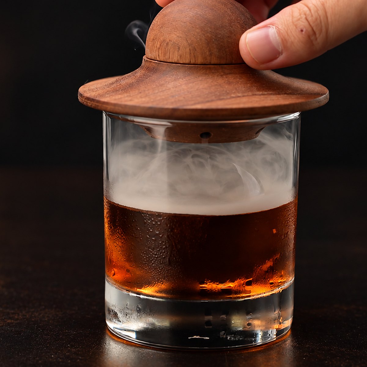 Placing the wooden smoker lid over the glass to infuse the drink