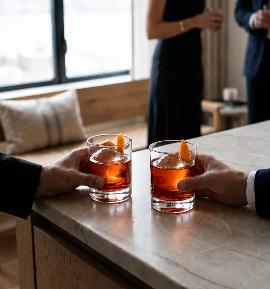 Two guests raising cocktails served over large clear ice spheres