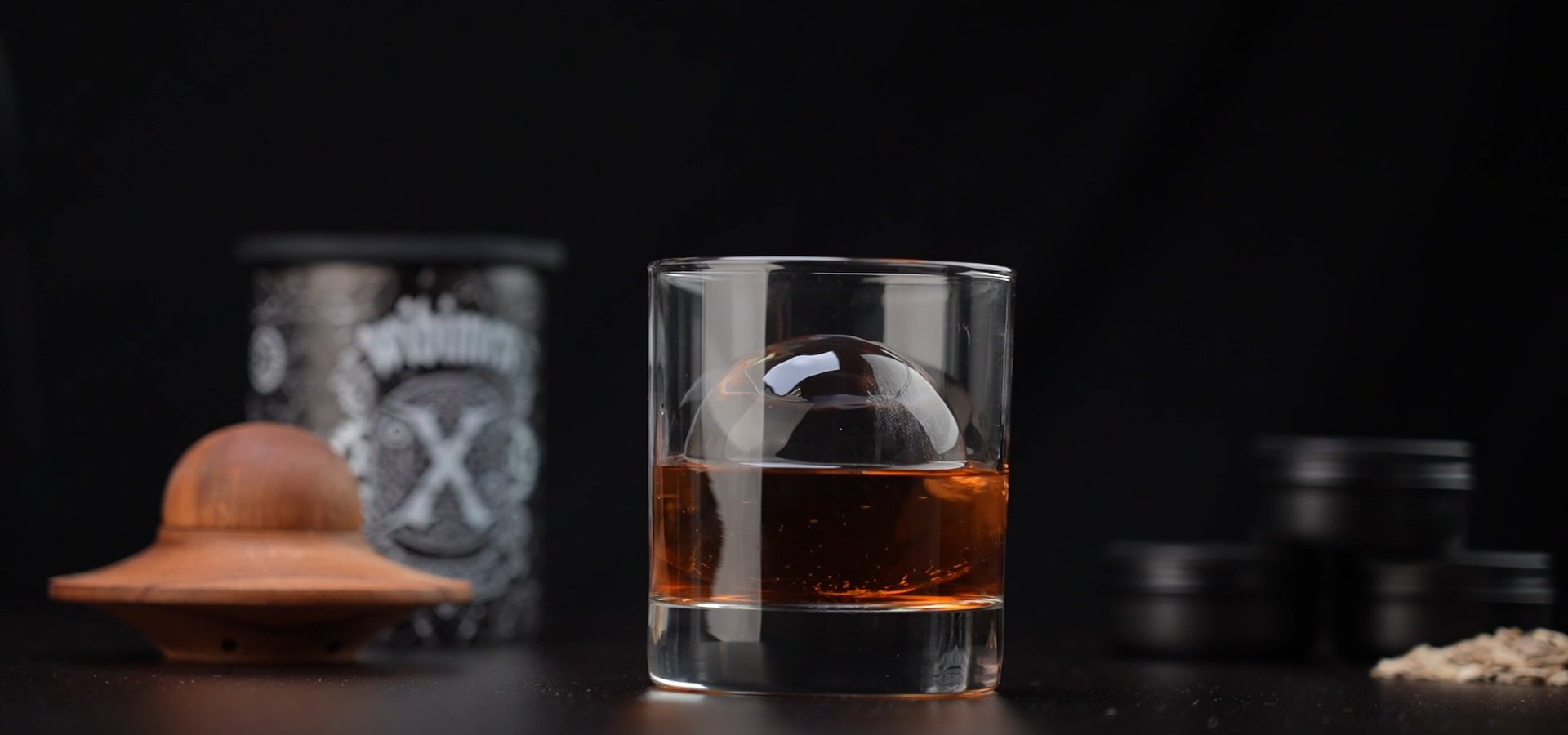 Whiskey with a large clear ice sphere in a dark home bar